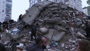 Menschen vor einem Schuttberg nach einem Erdbeben-Einsturz im südtürkischen Adana © Screenshot 