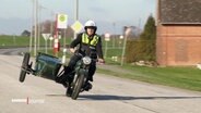 Der Polizist, der für Ochsenwerder zuständig ist, fährt auf einer Deichstrasse mit einem Motorrad mit Beiwagen © Screenshot 
