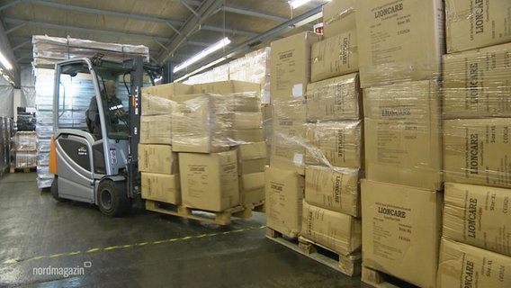 Ein Gabelstapler transportiert in einer Lagerhalle mit vielen Kartons einen Stapel weiterer Kartons. © Screenshot 