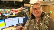 Moderator Michael Thürnau steht im Radiostudio, trägt ein Partyhütchen und grinst in die Kamera. © Screenshot 