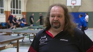 Ein Mann im Interview in einer Sporthalle, im Hintergrund spielen andere Tischtennis. © Screenshot 