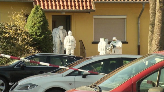 Mehrere Menschen in weißen Schutzanzügen vor einem Wohnhaus. © Screenshot 