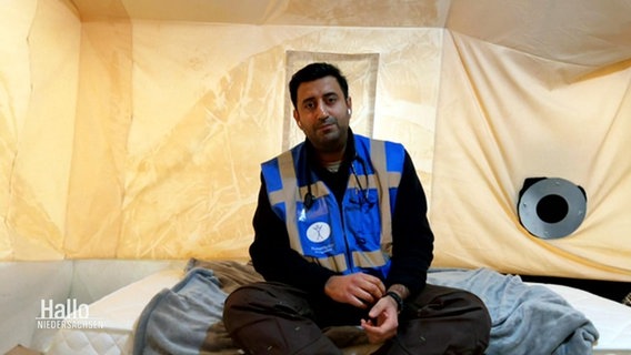 Ein Mann sitzt in einem Zelt: Der Arzt Wjahat Waraich aus Hannover. © Screenshot 