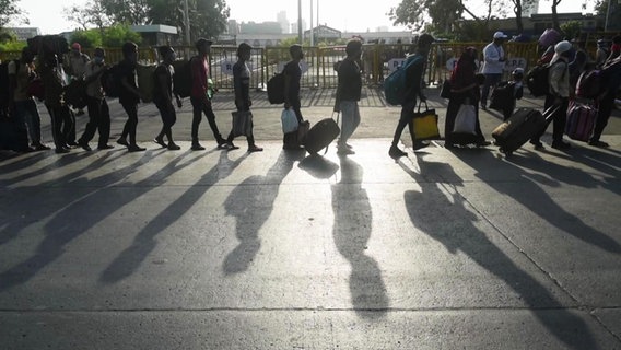 Viele Menschen mit Gepäck laufen in einer langen Reihe eine Straße entlang. © Screenshot 