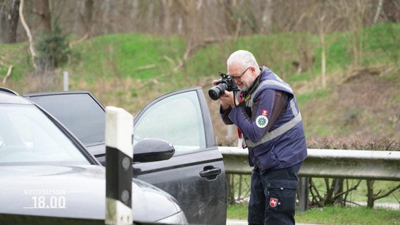 Ein Polizist fotografiert das Innere eines scharzen PKW © Screenshot 