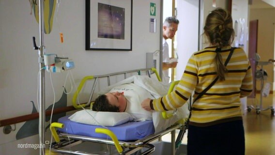 Ein Kind liegt auf einem Krankenhausbett in einem Klinikflur, eine Frau steht daneben. © Screenshot 