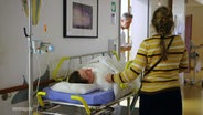 Ein Kind liegt auf einem Krankenhausbett in einem Klinikflur, eine Frau steht daneben. © Screenshot 