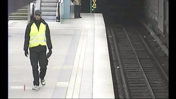 Bild einer Überwachungskamera in einer U-Bahnstation: Ein Mann zwischen 20-40 Jahren in dunkler Kleidung mit Baseballkappe und gelber Warnweste, ca. 1,8m groß. Er wird von der Polizei gesucht. © Screenshot 