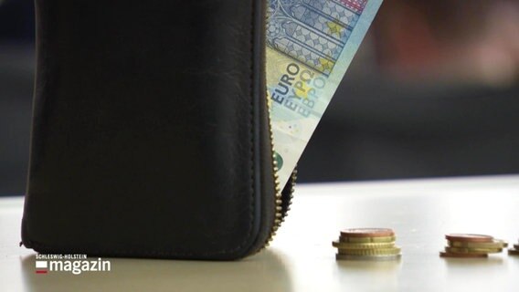 Eine offene Geldbörse, aus der ein 20 Euro-Schein herausragt, daneben ein paar Münzen. © Screenshot 