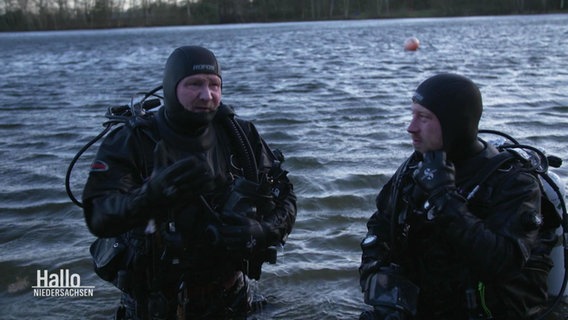 Zwei Personen in Tauchanzügen der Polizei stehen in einem Gewässer. © Screenshot 