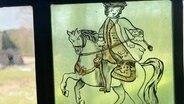 Auf einer grünlichen Fensterglasscheibe ist ein Reiter mit seinem Pferd abgebildet. © Screenshot 