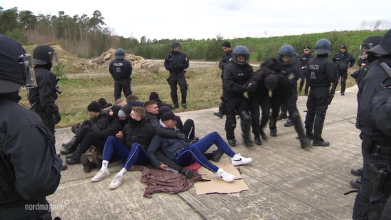 Polizisten in Schutzkleidung versuchen, bei einer Übung eine Sitzblockade aufzulösen. © Screenshot 
