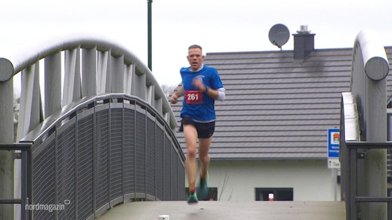 Ein Läufer läuft bei einem Wettkampf über eine kleine Fußgängerbrücke. © Screenshot 