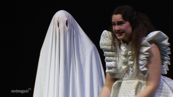 Eine Frau im weißen Kleid steht neben einem Gespenst. © Screenshot 