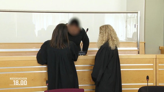 Ein Angeklagter steht mit seinen Anwältinnen im Gerichtssaal. © Screenshot 