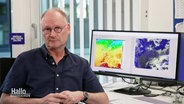 Meteorologe Sven Plöger sitzt an einem Schreibtisch mit einem Bildschirm, der eine Wetterkarte zeigt. © Screenshot 