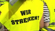 Gelbe Warnweste mit der Aufschrift "Wir streiken!" auf dem Rücken. © Screenshot 