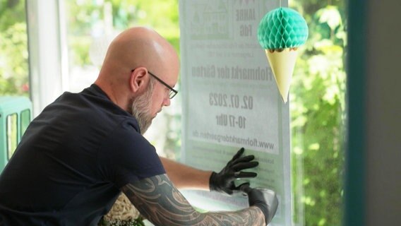 Ein Mann klebt ein Poster in die Scheibe einer Eisdiele. © Screenshot 