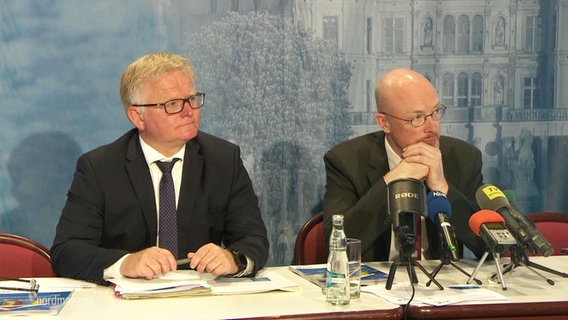 Zwei Männer sitzen an einem Tisch mit Mikrofonen und schauen nach rechts. © Screenshot 