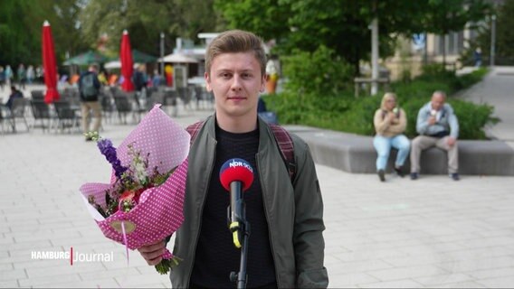 Jan Seibelt erklärt, wer für ihn die Hamburgerin des Tages ist. In seiner rechten Hand hält er einen Blumenstrauß. © Screenshot 