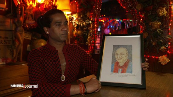 Satesh Mourya-Guthmann hält ein Portrait des ehemaligen Besitzers der Bar Crazy Horst. © Screenshot 
