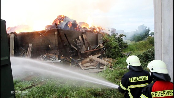 Feuerwehrleute löschen eine brennende Lagerhalle. © Screenshot 