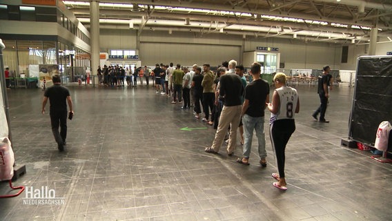 Viele Menschen warten in einer Schlange in einer Halle. © Screenshot 