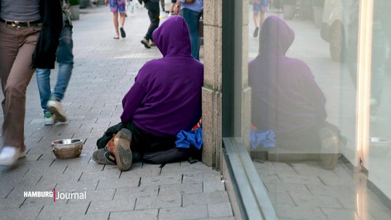 Eine Person sitzt auf der Straßen neben Fußgängern. © Screenshot 