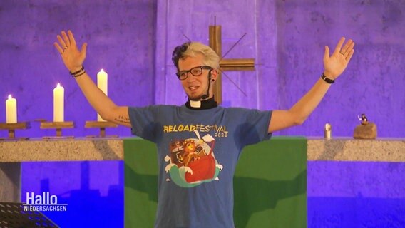 Person auf einem Altar hebt die Arme. Im Hintergund ein Kreuz. © Screenshot 