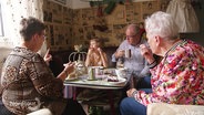 Menschen sitzen um einen Tisch und essen Kuchen in einem bunt dekoriertem Cafe. © Screenshot 
