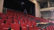 Reihen von roten Stühle stehen in einem großen Saal. © Screenshot 