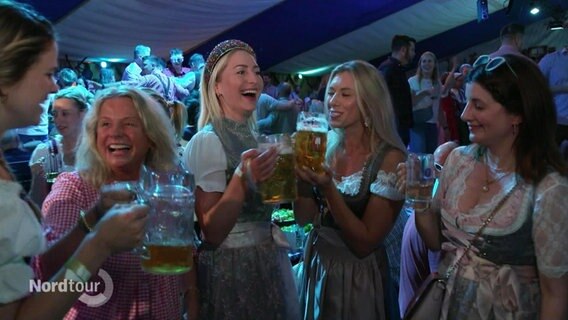 Frauen in Dirndln trinken in einem Festzelt aus großen Bierkrügen. © Screenshot 