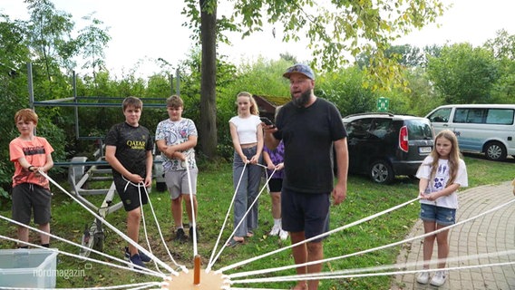 Kinder stehen bei einem Geschicklichkeitsspiel im Kreis, jeder hat ein Seil in der Hand, was zur Mitte führt. © Screenshot 