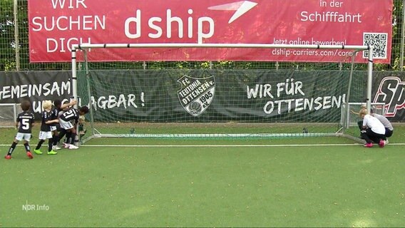 Kinder und Erwachsene versuchen ein großes Fußballtor auf einem Spielfeld anzuheben. © Screenshot 