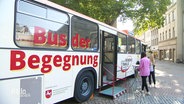 In einer Fußgängerzone ist ein Bus geparkt mit der Aufschrift "Bus der Begegnung". © Screenshot 