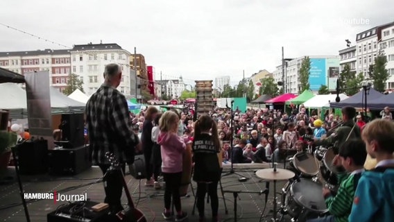 Menschen auf einer Bühne und ein Publikum davor unter freiem Himmel. © Screenshot 