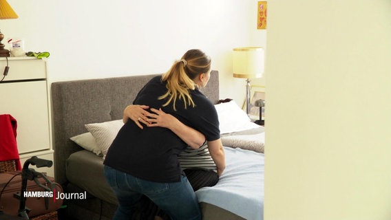 Eine Pflegerin hilft einer Frau auf die Beine. © Screenshot 