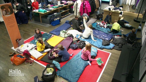 Kinder haben es sich auf Matratzen und Isomatten in Schlafsäcken in einer Ecke eines Bekleidungsgeschäfts gemütlich gemacht. © Screenshot 