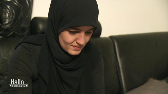 Eine Frau mit Hijab sitzt auf einem Sofa und blickt, etwas lesend, vor sich hinunter. © Screenshot 