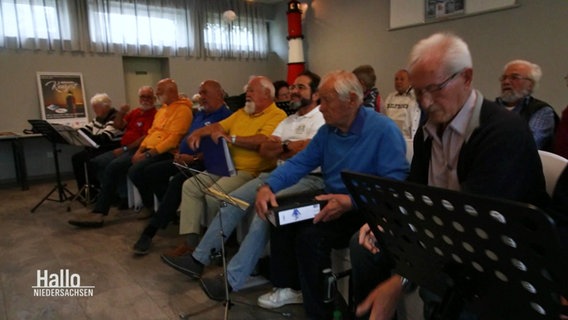 Viele älterere Menschen sitzen bei einer Chorprobe in einem Raum eines Vereinsheims. © Screenshot 