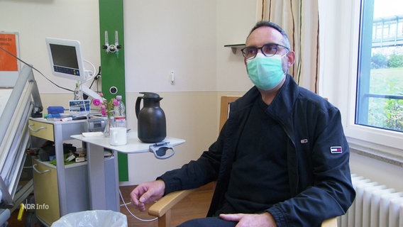 Ein Mann trägt in einem Krankenhauszimmer einen Mundschutz. © Screenshot 