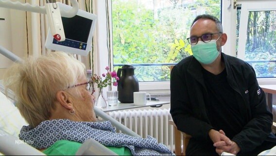 Eine Person mit Maske sitz am Bett einer Patientin. © Screenshot 