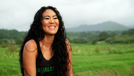 Eine Profilaufnahme einer lächelnden Frau, im Hintergrund eine grüne, hügelige Landschaft. © Screenshot 