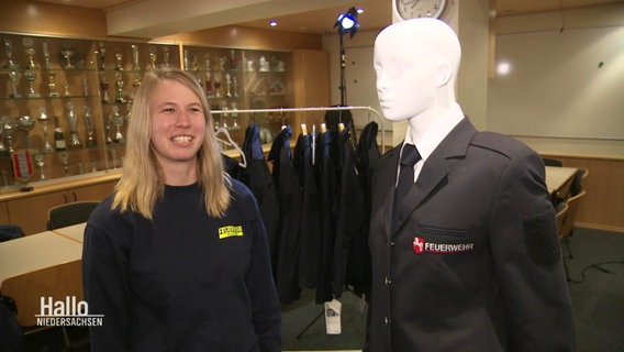 Eine lächelnde Person neben einem Manika mit einer Uniform. © Screenshot 
