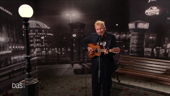 Robert Stadlober mit Akkustikgitarre und Mikrofon vor schwarzem Hintergrund. © Screenshot 