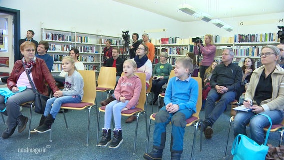 Kinder und Eltern sitzen auf Stühlen. © Screenshot 