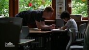 Ein Mann hilft einem Jungen in einem Klassenzimmer. © Screenshot 