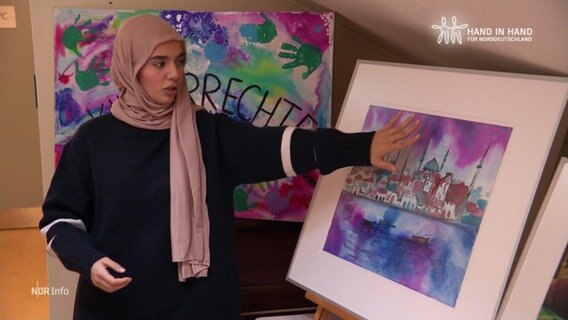 Die Jugendliche Mawadah Al-Rubaye vor zeigt ihr gemaltes Bild auf einer Staffelei. © Screenshot 