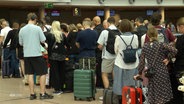 Menschen stehen mit Gepäck an der Gepäckabgabe am Flughafen. © Screenshot 
