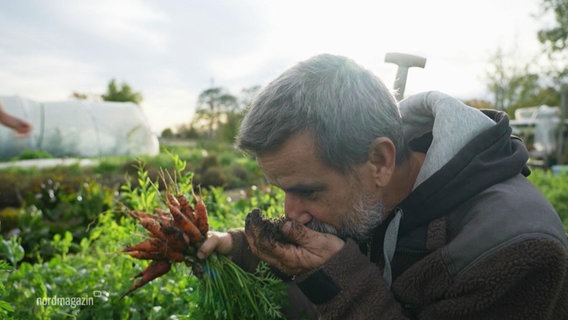 Ein Mann mit einem Bund Möhren in der Hand in seinem Garten richt an der Erde. © Screenshot 
